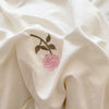 Close-up of a cream fabric with a delicate olive green branch and pink rose embroidery.
