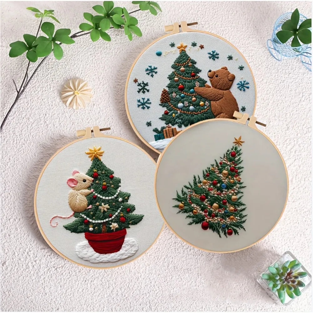 A hand embroidery kit featuring a Christmas tree with a bear and festive greenery on a round canvas.