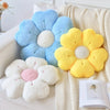 A collection of fluffy blue, yellow, and white daisy flower shaped throw pillows resting on a cream knitted blanket.