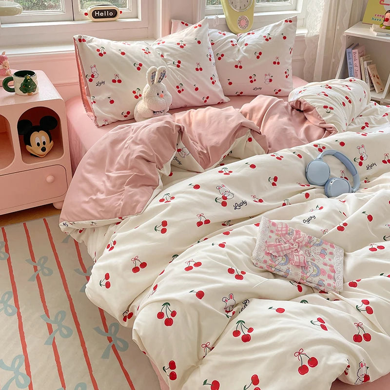 A pink and white duvet cover set with a cherry pattern and matching pillows on a bed.