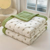 A stack of lightweight floral printed summer quilts in sage green and cream fabric.