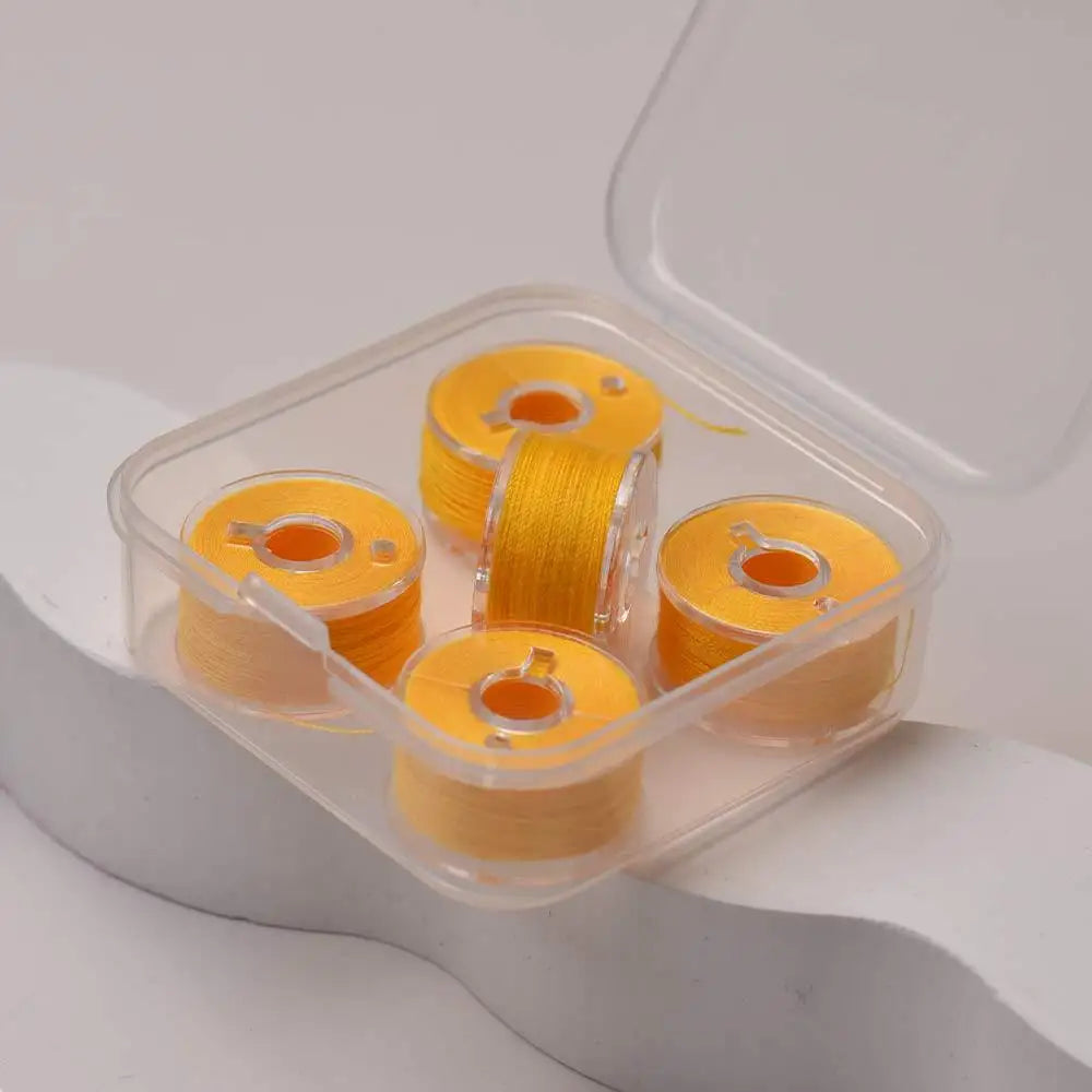 A clear plastic container holds several spools of yellow prewound sewing machine bobbin threads.