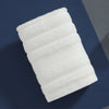 A stack of four white, ribbed pure cotton face towels for kids and adults placed on a dark blue surface.