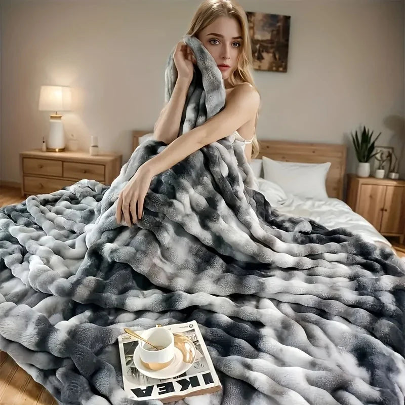A gray and white plush faux rabbit fur throw blanket draped over a bed in a bedroom setting.
