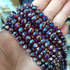 A hand holds a cluster of faceted, deep purple and blue iridescent glass beads for crafting.