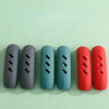 A row of silicone pan handle covers in various shades of gray, teal, and red are displayed on a light green surface.