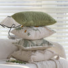 A stack of embroidered floral cushion covers in sage green, cream, and beige resting on a light-colored fabric.