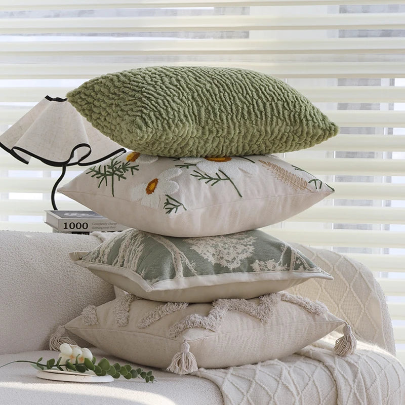 A stack of embroidered floral cushion covers in sage green, cream, and beige resting on a light-colored fabric.