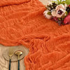 Orange ruffled gauze table runner draped in soft folds with a floral arrangement