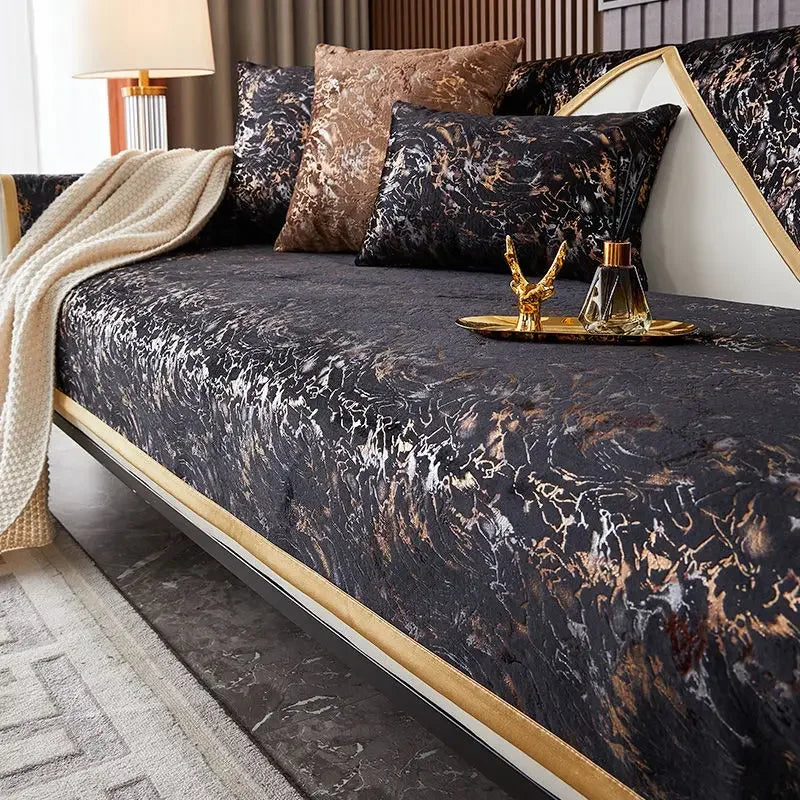 A dark velvet bed cover with gold leaf accents and a beige throw blanket on a modern bed.