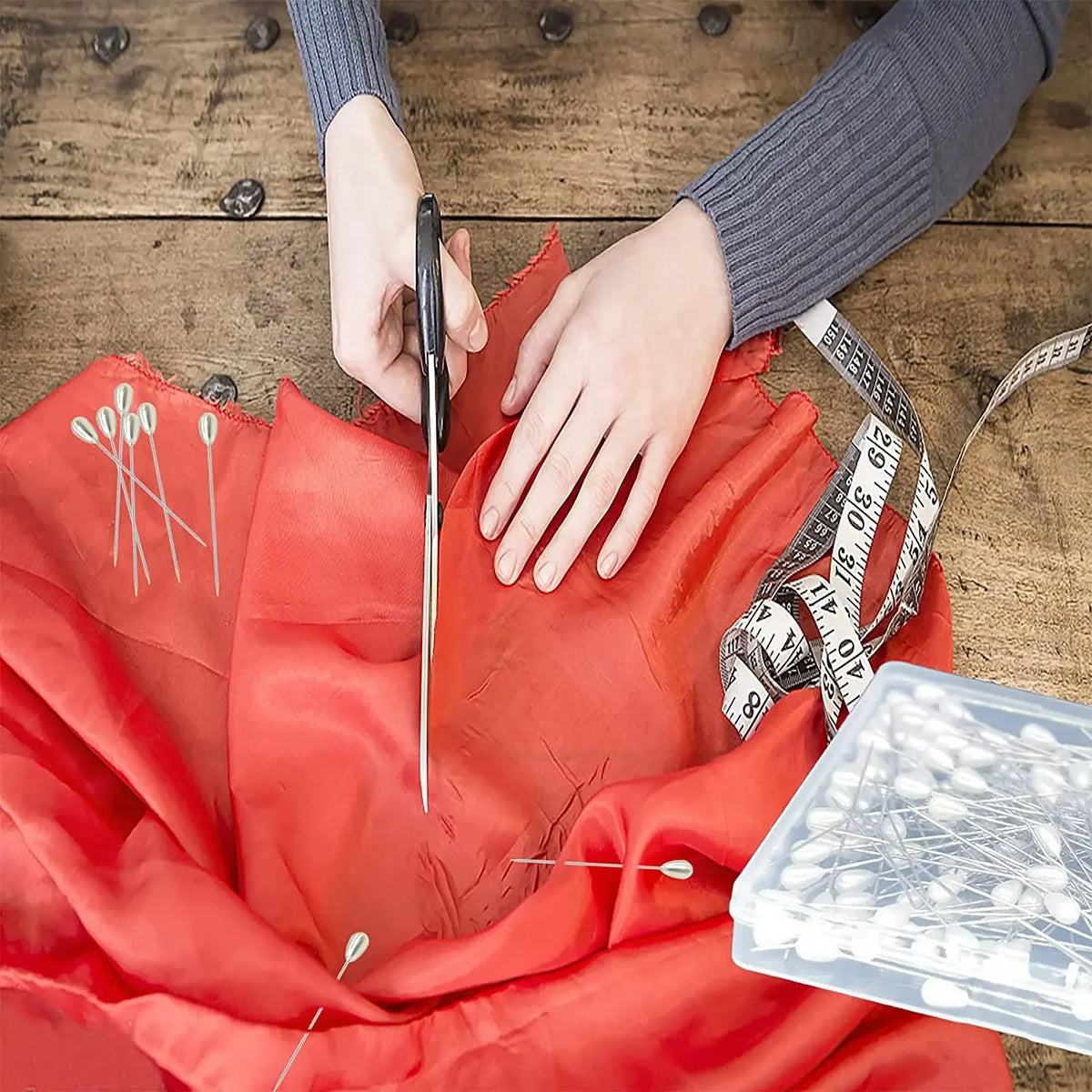 Hands are pinning a red fabric with sewing pins and a measuring tape for crafting.