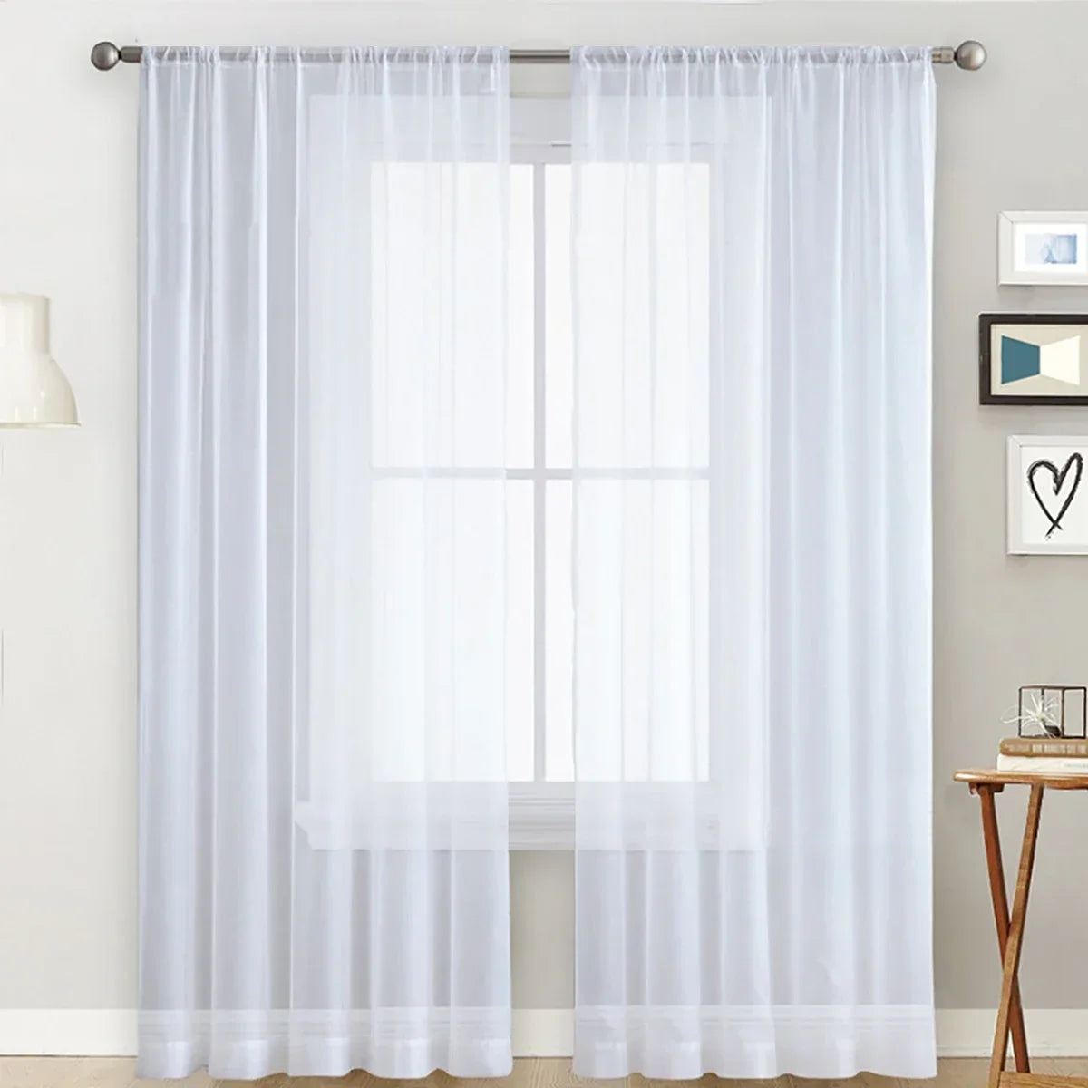 White sheer curtain with a rod pocket hanging over a window in a living room setting.