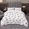 A white duvet cover set featuring a repeating pattern of red and green fruit leaves on a gray upholstered bed.