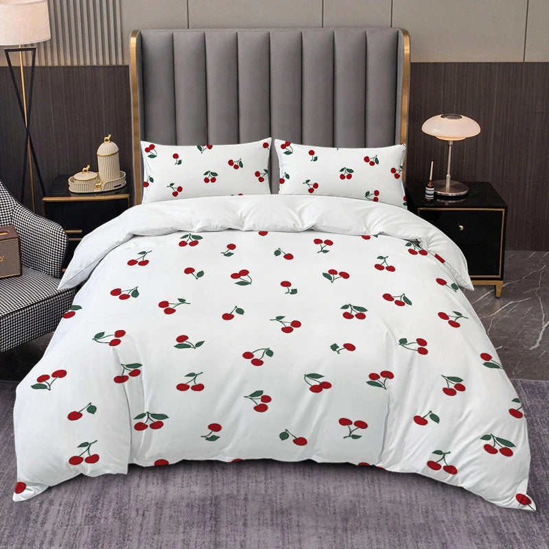 A white duvet cover set featuring a repeating pattern of red and green fruit leaves on a gray upholstered bed.