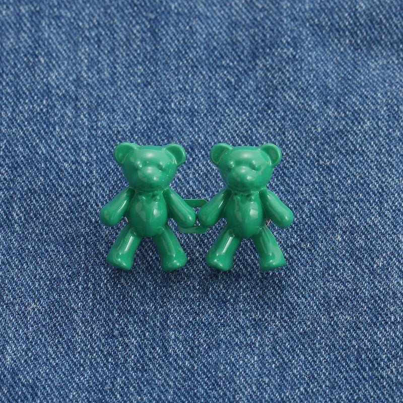 Two small, green bear button pins are displayed on a blue denim fabric.