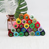 A collection of 24 handmade sewing threads in various colors and shades arranged on a white surface.
