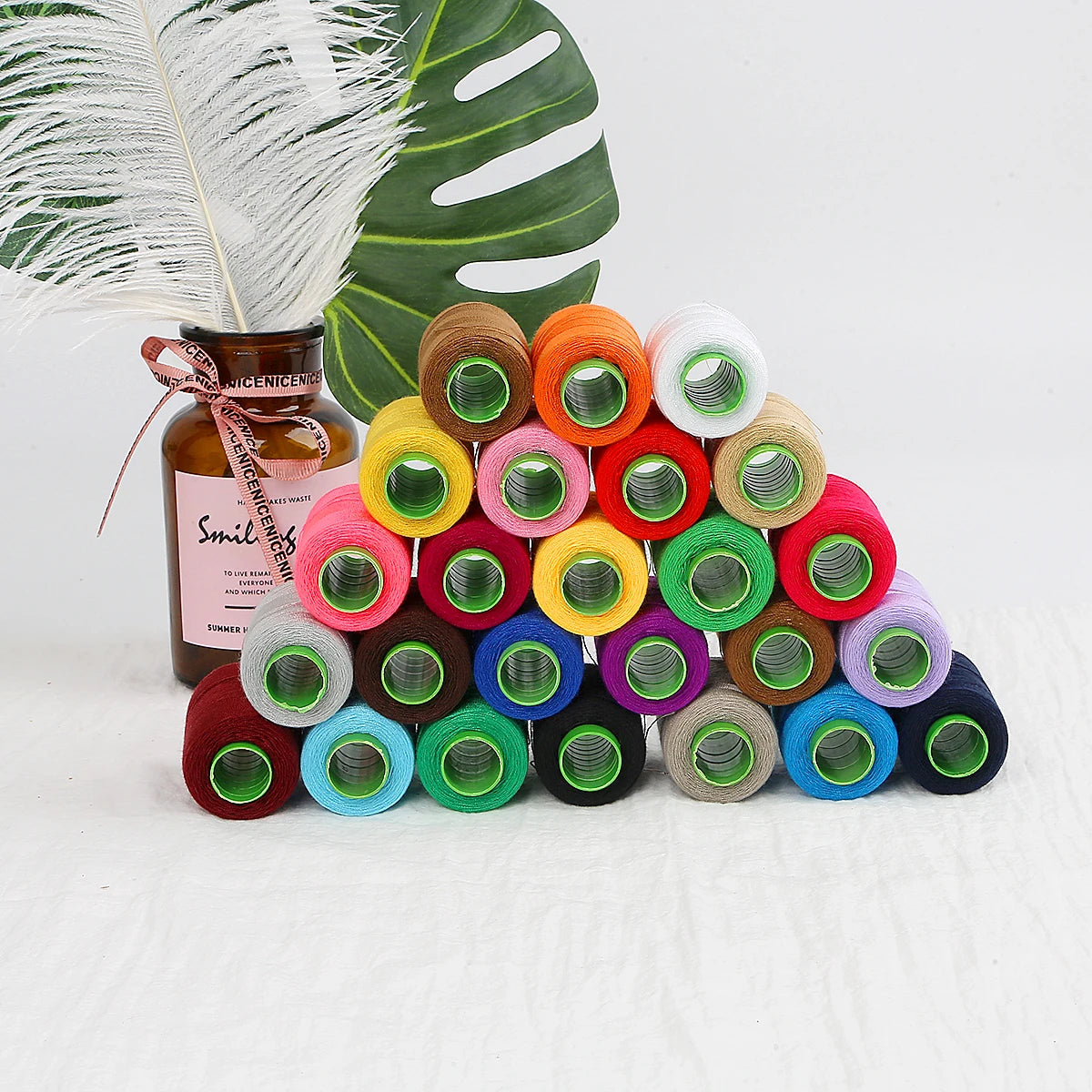 A collection of 24 handmade sewing threads in various colors and shades arranged on a white surface.