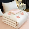 A white embroidered cooling summer quilt with pink floral designs and a matching pink pillow is displayed on a light pink sur