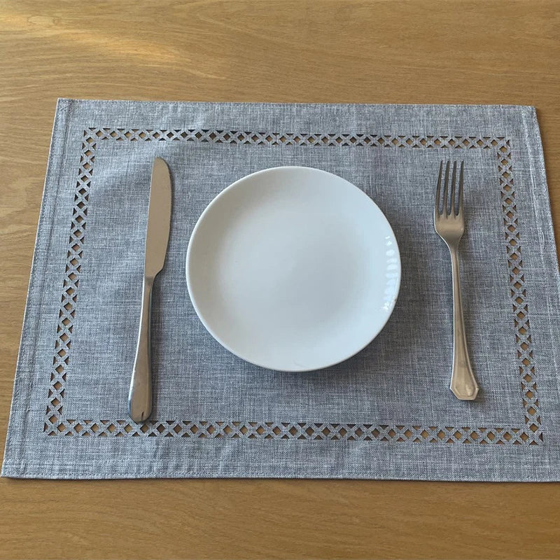 A place setting featuring a white plate, knife, and fork on a gray linen placemat.