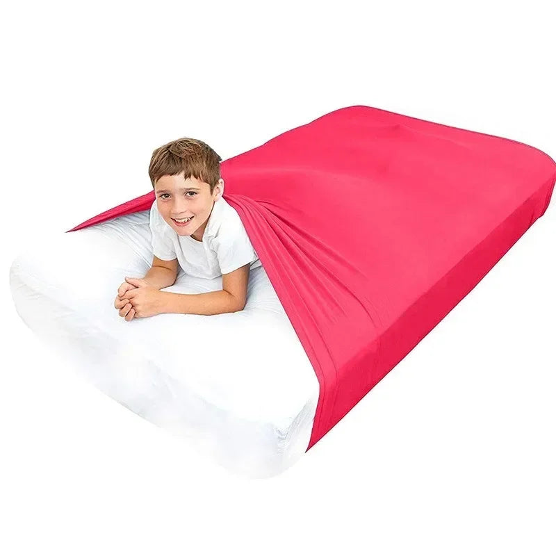 A young boy smiling while lying on a white sensory bed sheet covered by a bright pink breathable stretchy sheet.