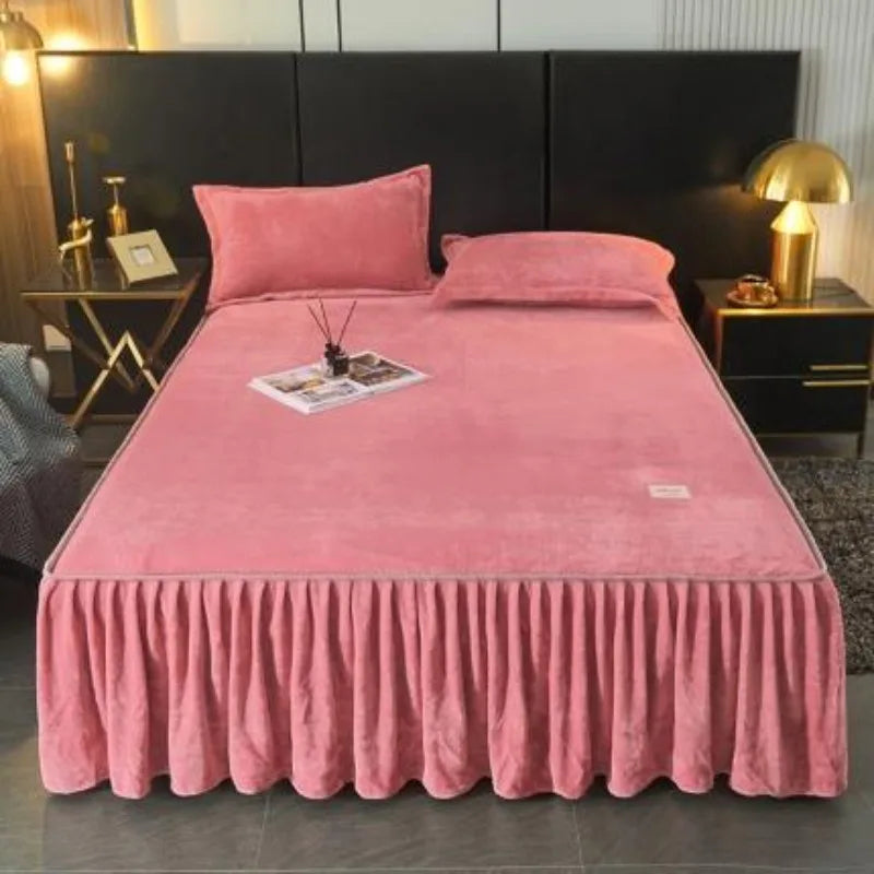 A thick pink velvet bed skirt with a ruffled hem and a matching pillow is displayed on a bed.