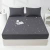 A dark gray waterproof mattress and bed protector sheet is laid over a mattress, with water droplets visible on the surface.
