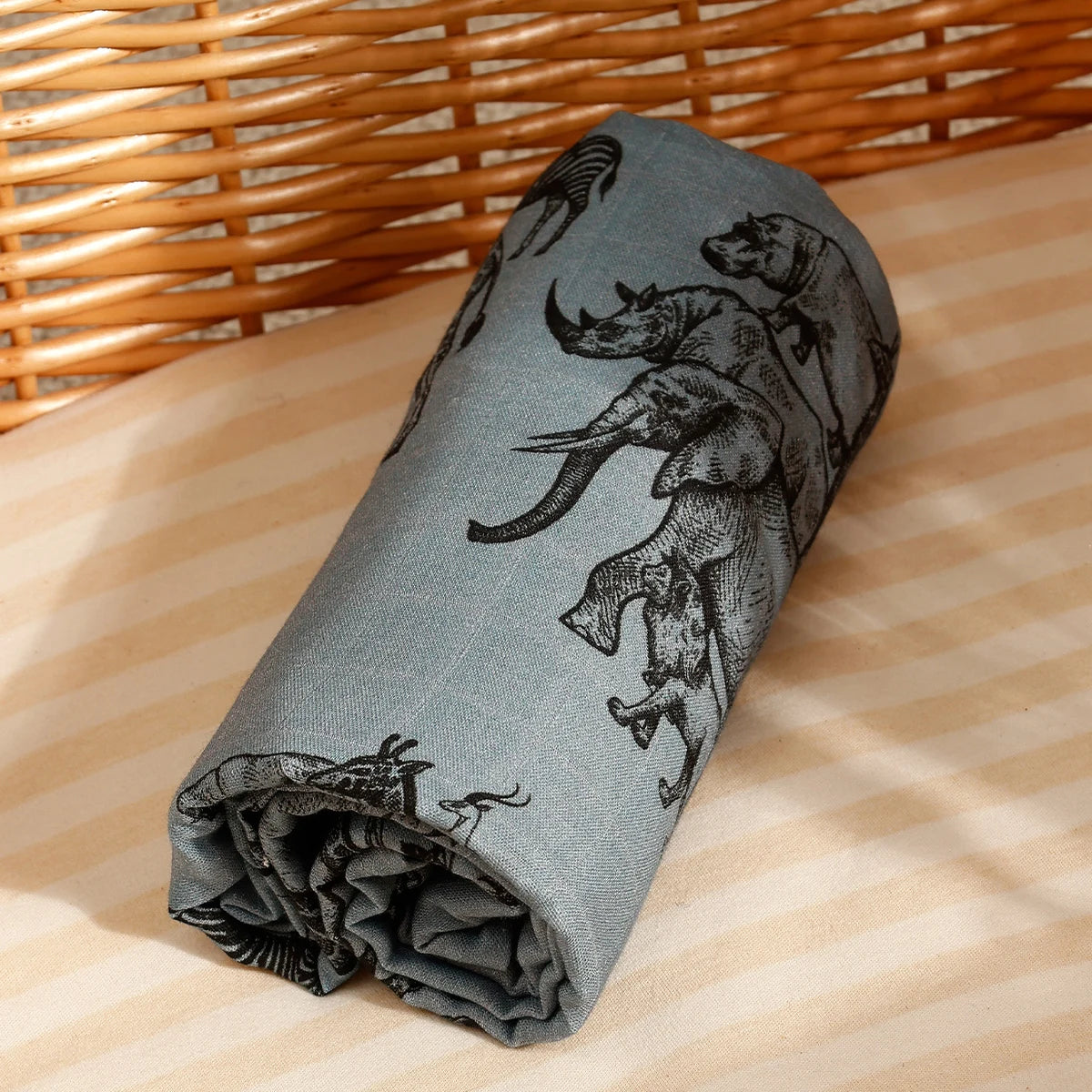A gray muslin swaddle blanket featuring black silhouette illustrations of various animals.