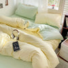 A bed covered with a light green duvet and yellow bedding, featuring white pillows and a black label.