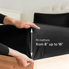 A hand adjusts a black fitted mattress cover on a wooden bed frame.