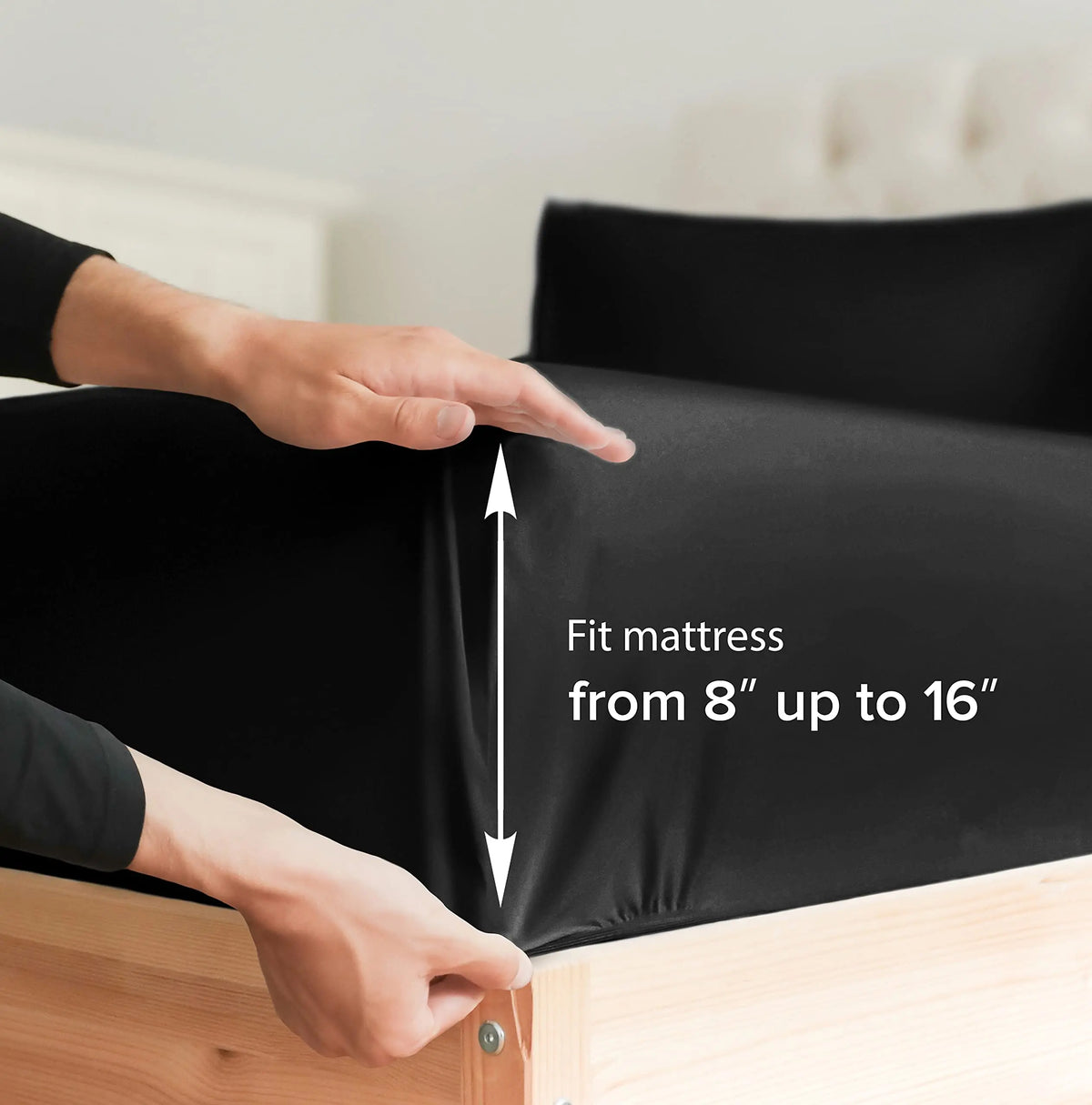 A hand adjusts a black fitted mattress cover on a wooden bed frame.