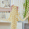 A hand is holding a decorative fabric door curtain with tassel trim, featuring yellow and cream beads.