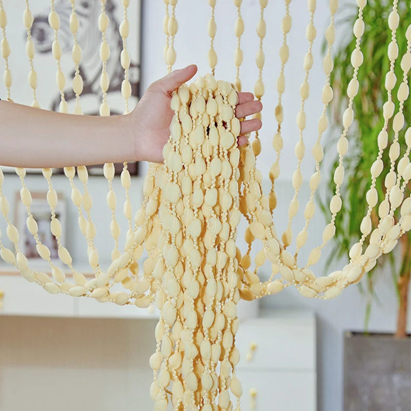 A hand is holding a decorative fabric door curtain with tassel trim, featuring yellow and cream beads.