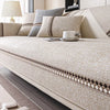 A beige linen sofa cover with decorative trim is displayed on a modern sofa in a living room setting.