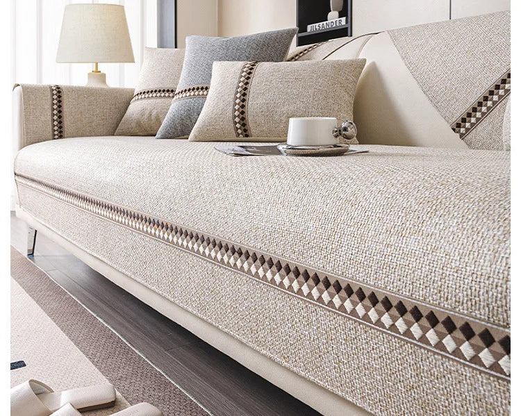 A beige linen sofa cover with decorative trim is displayed on a modern sofa in a living room setting.