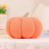An orange fuzzy 3D pumpkin shaped throw pillow with a silver stem, displayed on a white lace surface.