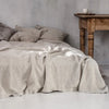 A beige pure linen flat sheet draped over a bed in a minimalist room with wooden furniture.