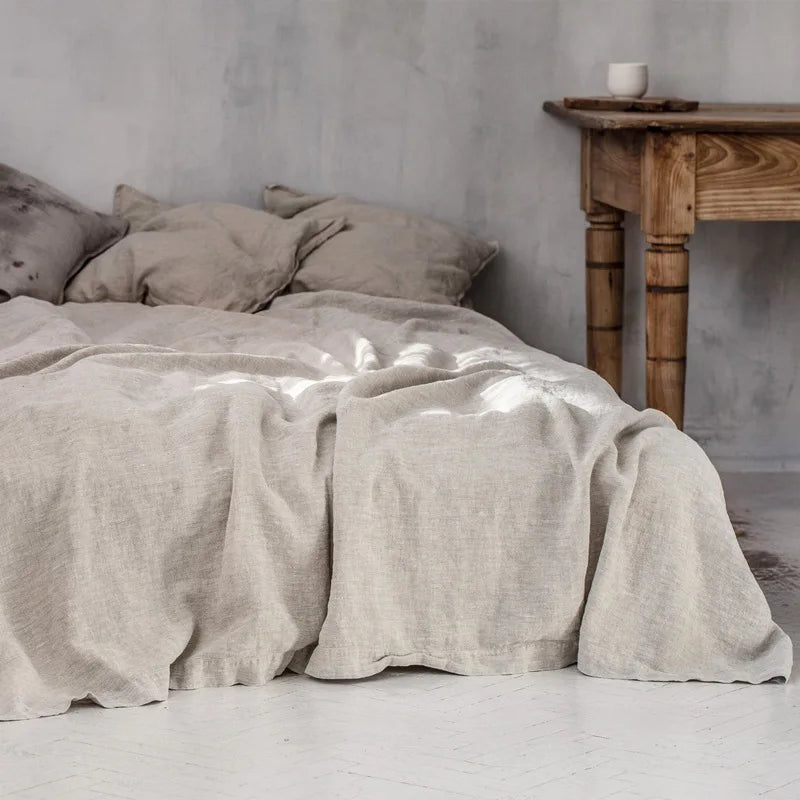 A beige pure linen flat sheet draped over a bed in a minimalist room with wooden furniture.