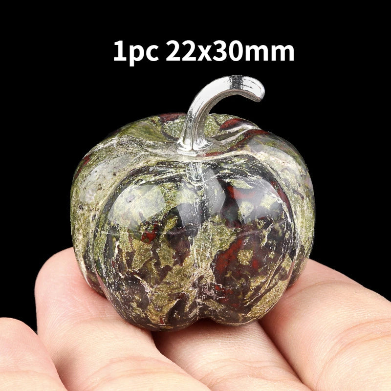 A natural stone pumpkin figurine with a textured, mottled green and brown appearance is held in a hand.