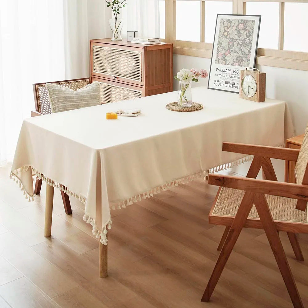A light beige table is set with textured cotton tassel runners, wood furniture, and a glass vase of flowers.