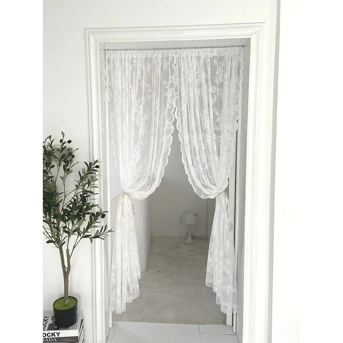 A pair of sheer white floral embroidery curtains hanging in a white framed doorway.