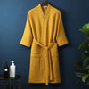 A mustard yellow cotton terry robe hanging on a dark blue wall.