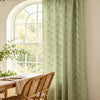Sage green floral print curtains hanging in a bright room next to a wooden table and chairs.
