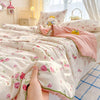 A hand is holding a pink and white floral quilt with pink trim on a bed.