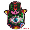A black iron-on patch featuring a pink and green design with a central blue eye made of sequins.