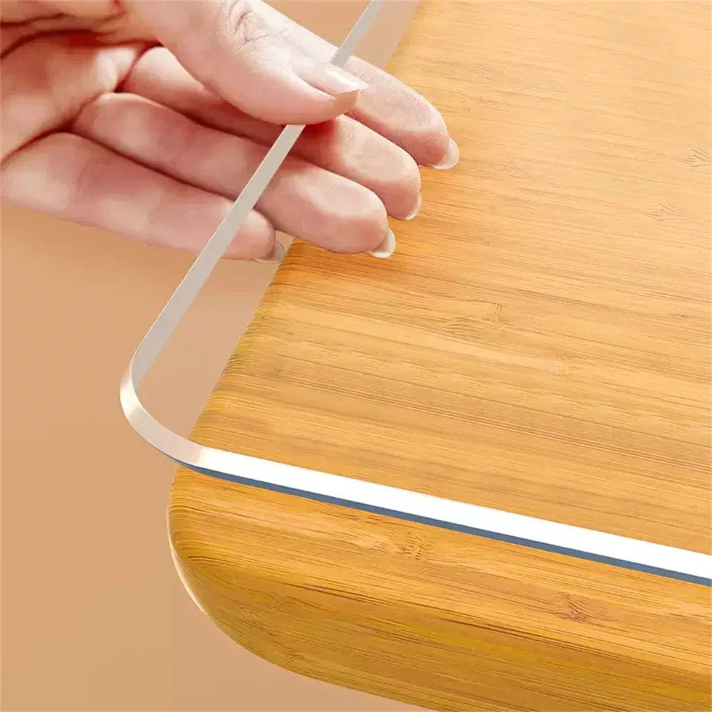 A hand is placing a clear PVC table protector mat onto a wooden surface.