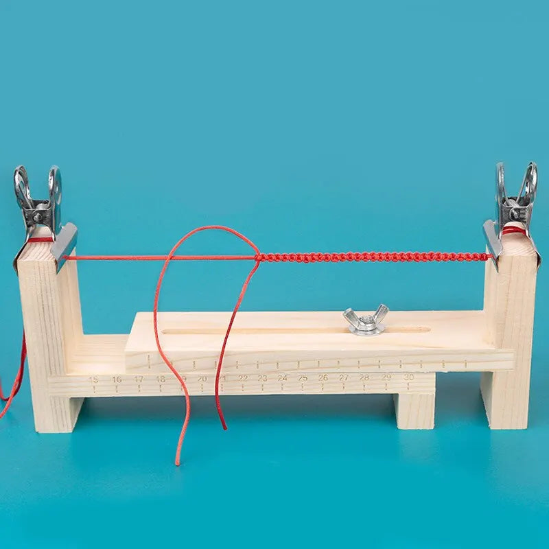 A wooden braiding frame with pliers and a red cord is displayed on a blue surface.