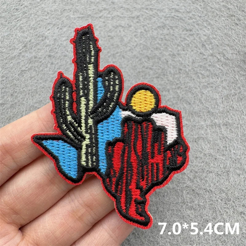 An embroidered iron-on patch featuring a stylized silhouette of a cowboy hat and landscape in red, blue, and black thread.