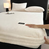 A white plush jacquard mattress cover is displayed on a black bed with white pillows and a bedside lamp.