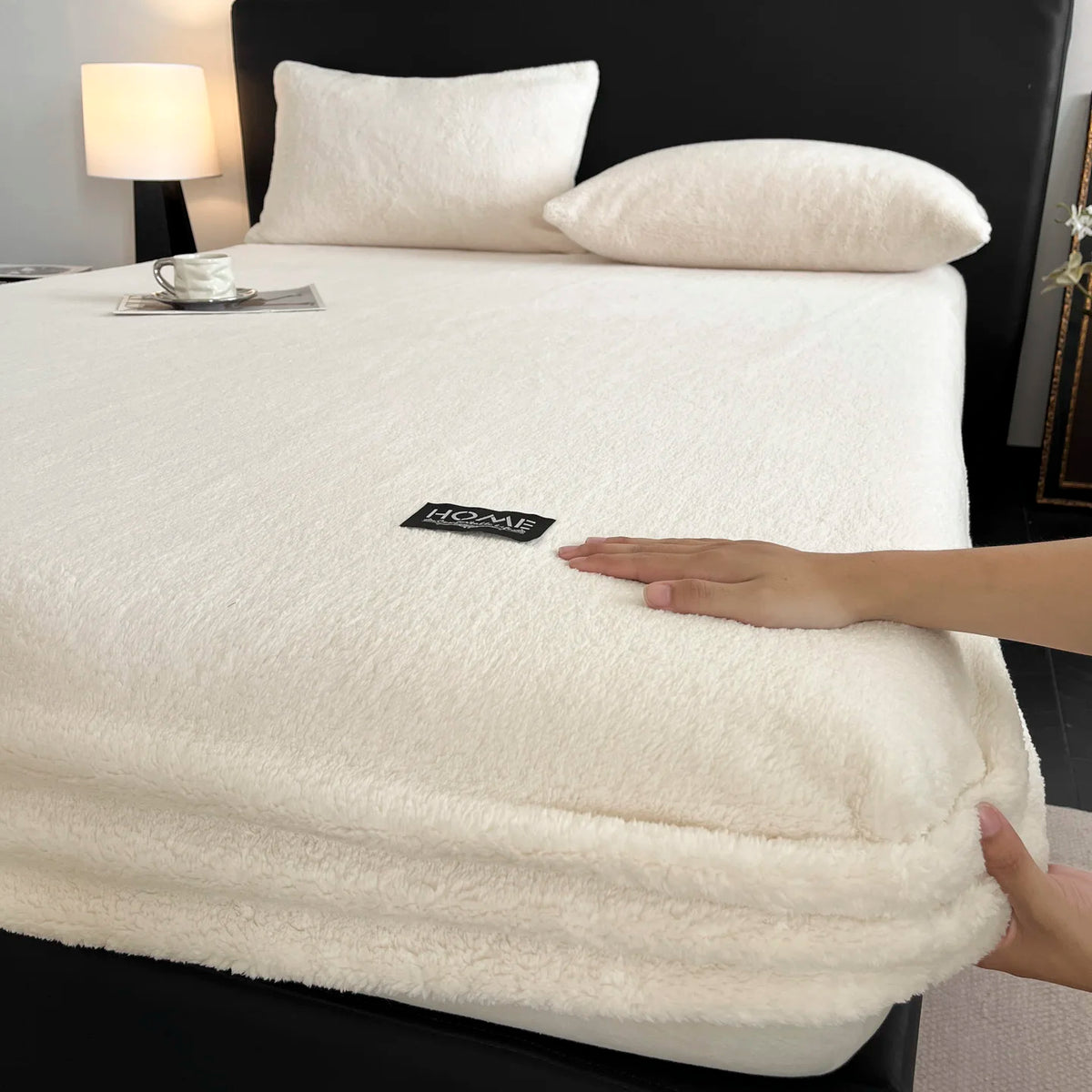 A white plush jacquard mattress cover is displayed on a black bed with white pillows and a bedside lamp.