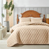 Light beige quilted bedding set with a wooden headboard and white linens in a bright room.